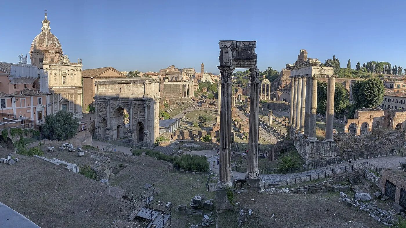 ローマのフォロ・ロマーノを東向きに見渡した実写。神殿の柱や凱旋門の遺跡が夕方の光に照らされている